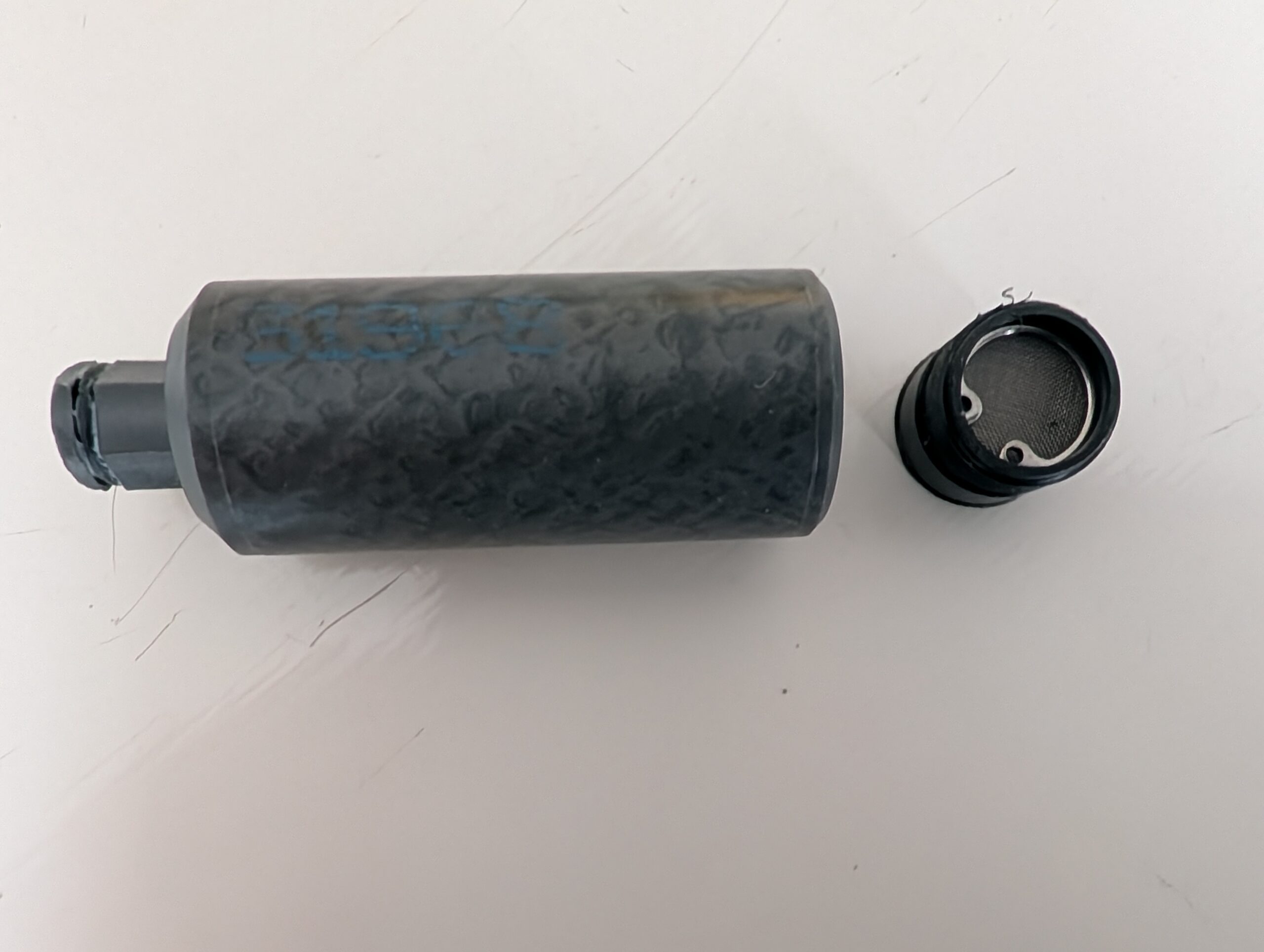 Black cylindrical object with a removable cap on a white surface.